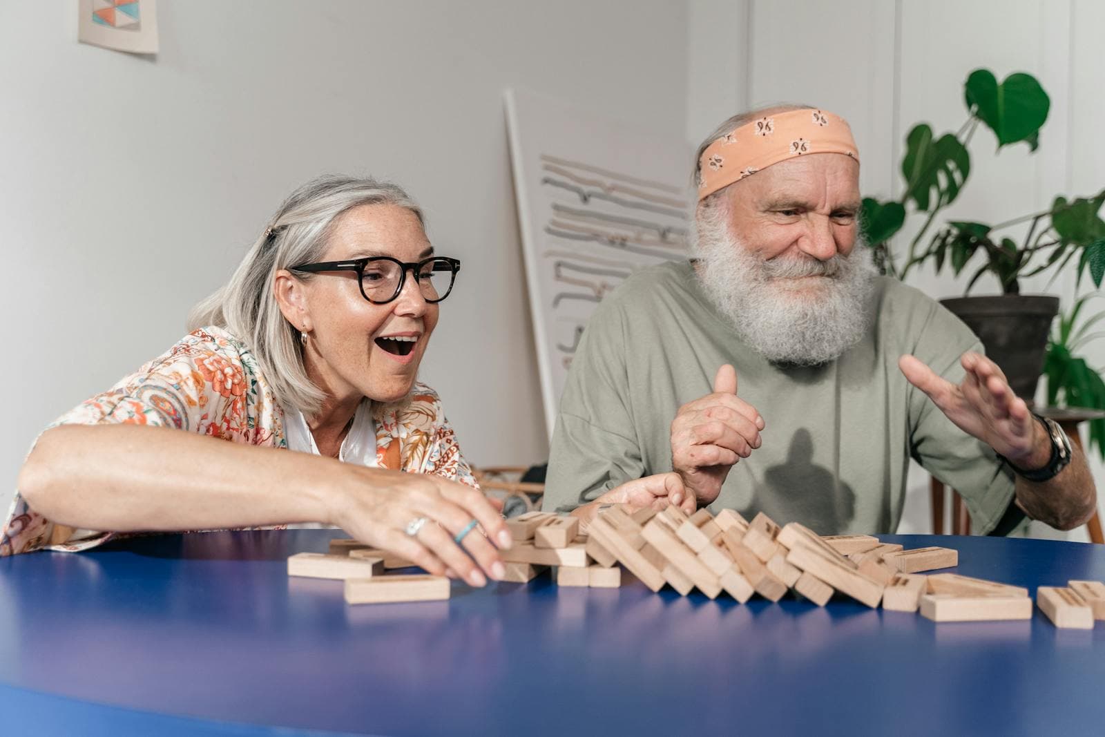 An elderly couple laughs and bonds while playing Jenga indoors — the everyday joy of senior companion care.