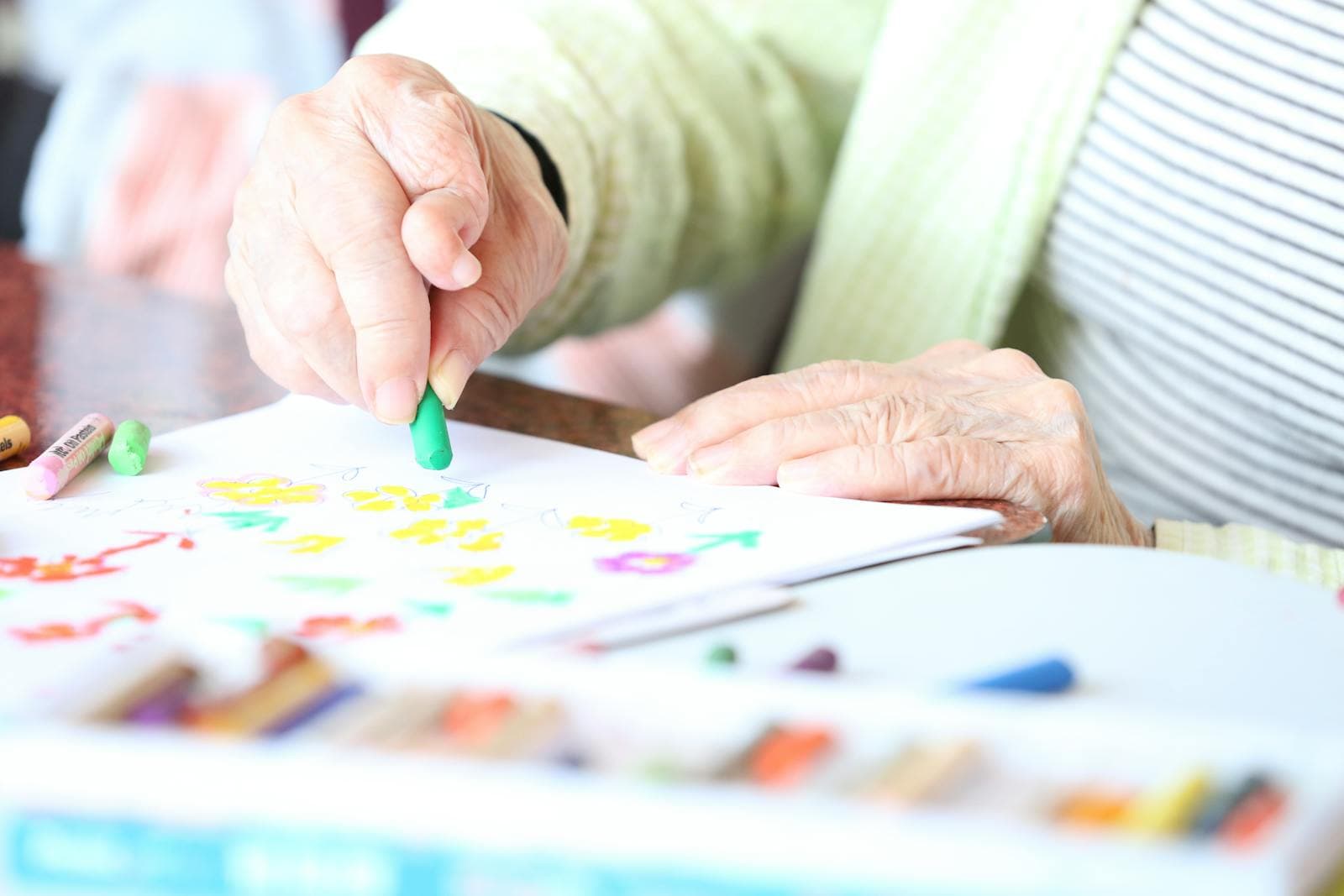 A senior participates in creative activity with crayons — companion-led hobby support.